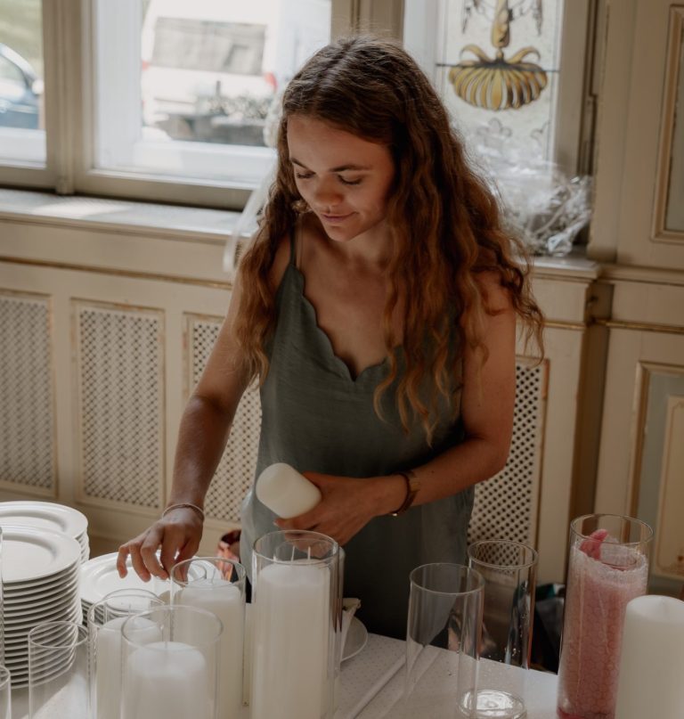 Hochzeitsplanerin Hannah von NeckarMomente sitzt lächelnd mit einem hellen Anzug und einem Plan in der Hand auf einem rosanem Stuhl.