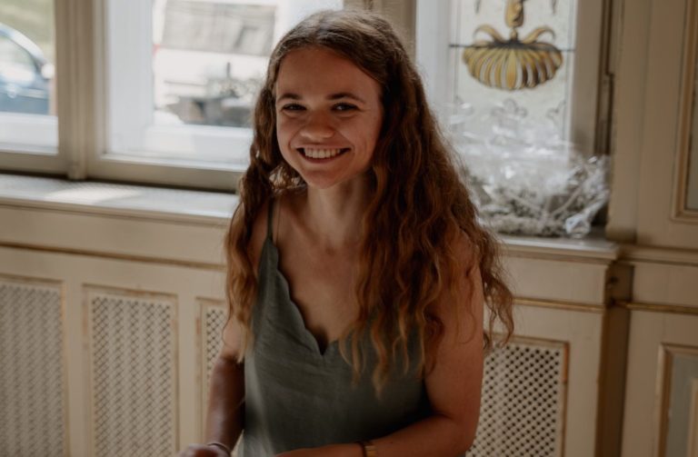 Hochzeitsplanerin Hannah in einem hellen Anzug die einen Holzstuhl auf einem Event hin und her herträgt.